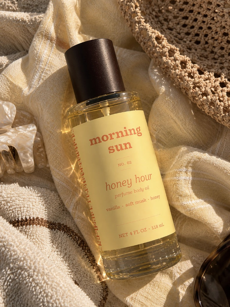 Honey Hour perfume body oil, no. 02, on a linen beach towel with a straw hat and claw clip