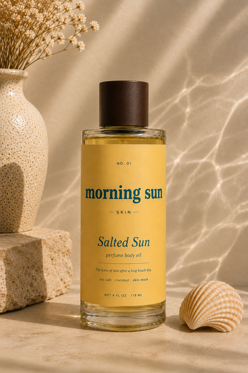Close-up of Salted Sun non-toxic perfume body oil bottle by Morning Sun, styled with dried flowers and a seashell on sunlit water.