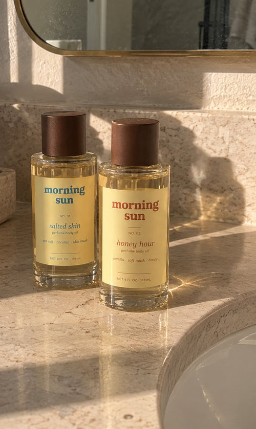 Salted Skin and Honey Hour perfume body oils on a sunlit bathroom vanity