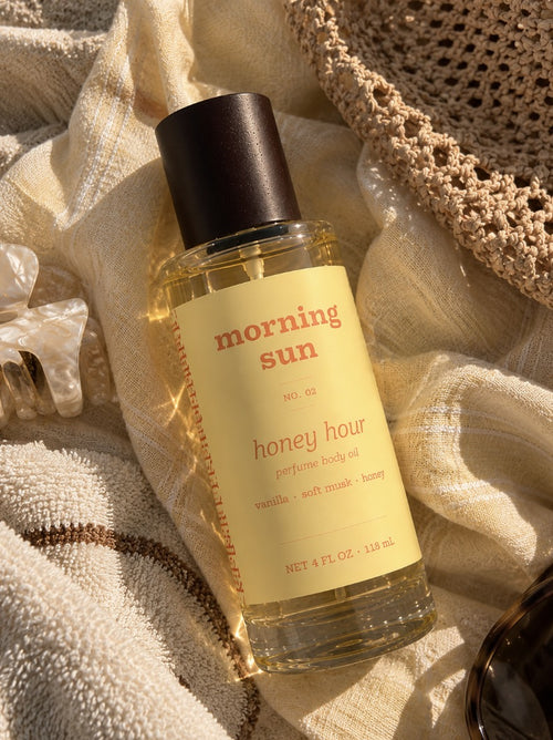 Honey Hour perfume body oil, no. 02, on a linen beach towel with a straw hat and claw clip