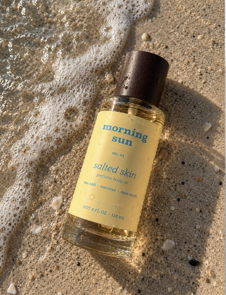 Salted Skin perfume body oil, no. 01, lying in wet sand at the shoreline as sea foam rolls in