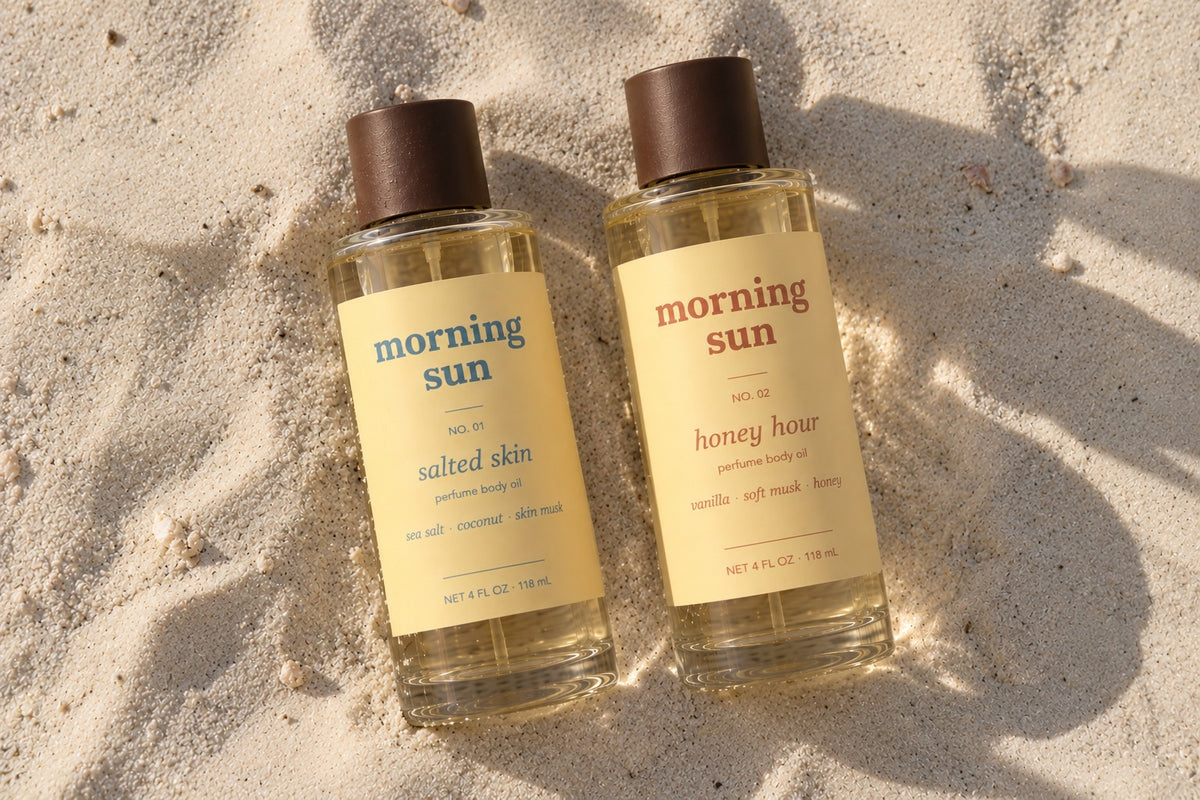 Salted Skin and Honey Hour perfume body oils side by side in sunlit beach sand