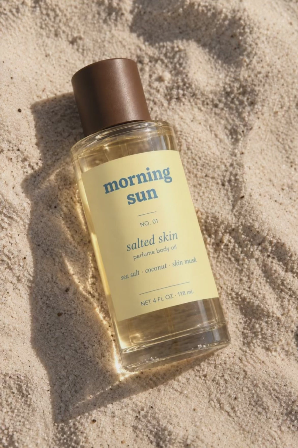 Salted Skin perfume body oil, no. 01, resting in beach sand as a wave washes over it